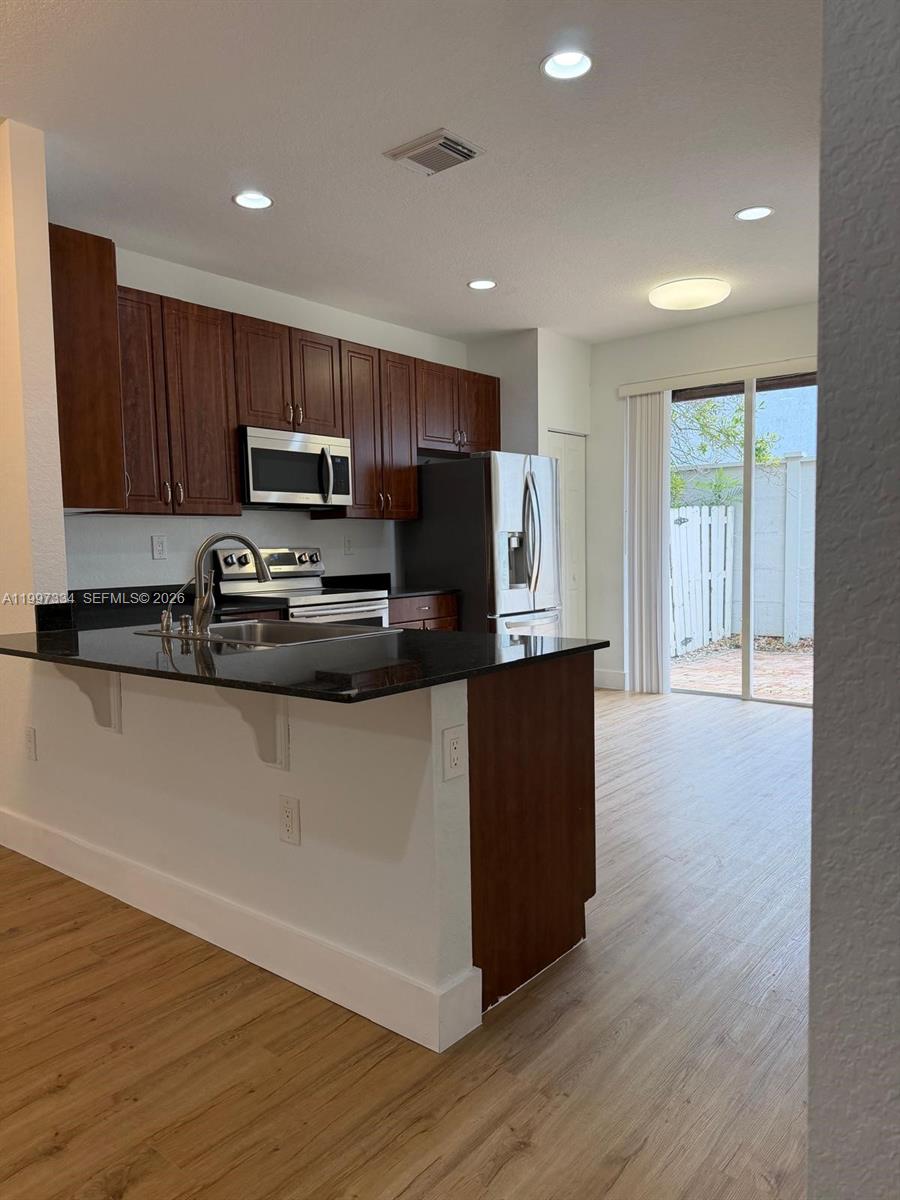 14934 Southwest 41st Lane, Unit 14934 Miami, FL 33185 - Photo 5 of 36 a kitchen with kitchen island granite countertop wooden cabinets a refrigerator a stove a microwave and wooden floor