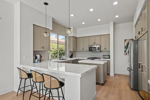 a kitchen with stainless steel appliances granite countertop a stove top oven a refrigerator a sink and chairs