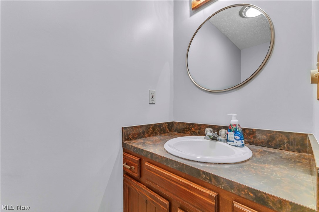 6635 Taylor Road Painesville, OH 44077 - Photo 15 of 41 Powder room featuring a wood-finish vanity with an integrated sink, a dark countertop, and a circular wall-mounted mirror