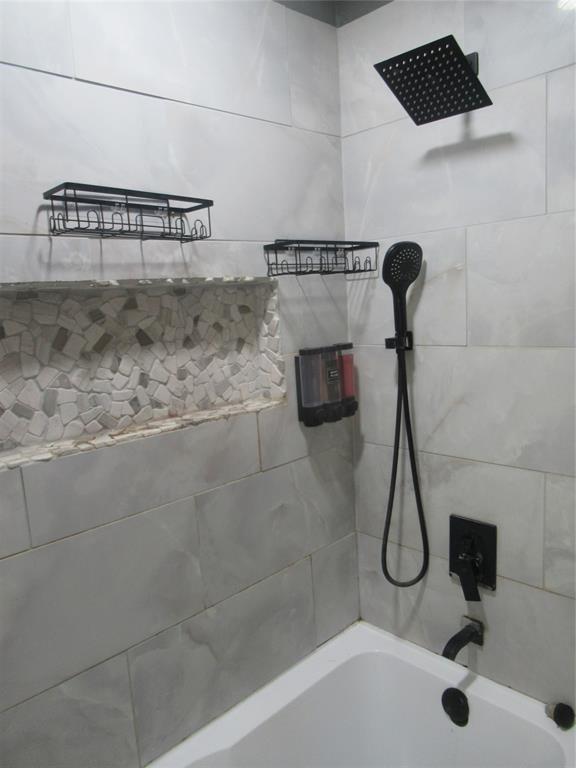 24133 Highway 157 Springhill, LA 71075 - Photo 17 of 19 Bathtub and shower combination featuring large format grey wall tiling, a stone mosaic shower niche, a matte black rainfall showerhead, and a matte black handheld shower