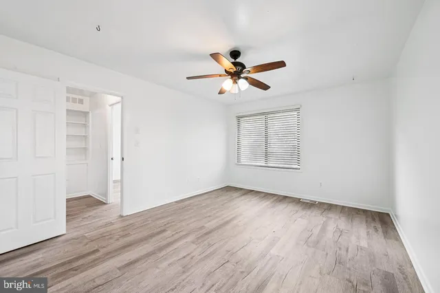 an empty room with wooden floor ceiling fan and windows