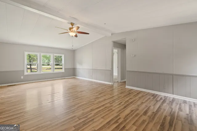 an empty room with wooden floor chandelier fan and windows