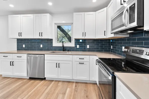 a kitchen with white cabinets a sink dishwasher and a stove with wooden floor