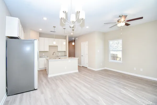 an empty room with wooden floor chandelier fan and windows