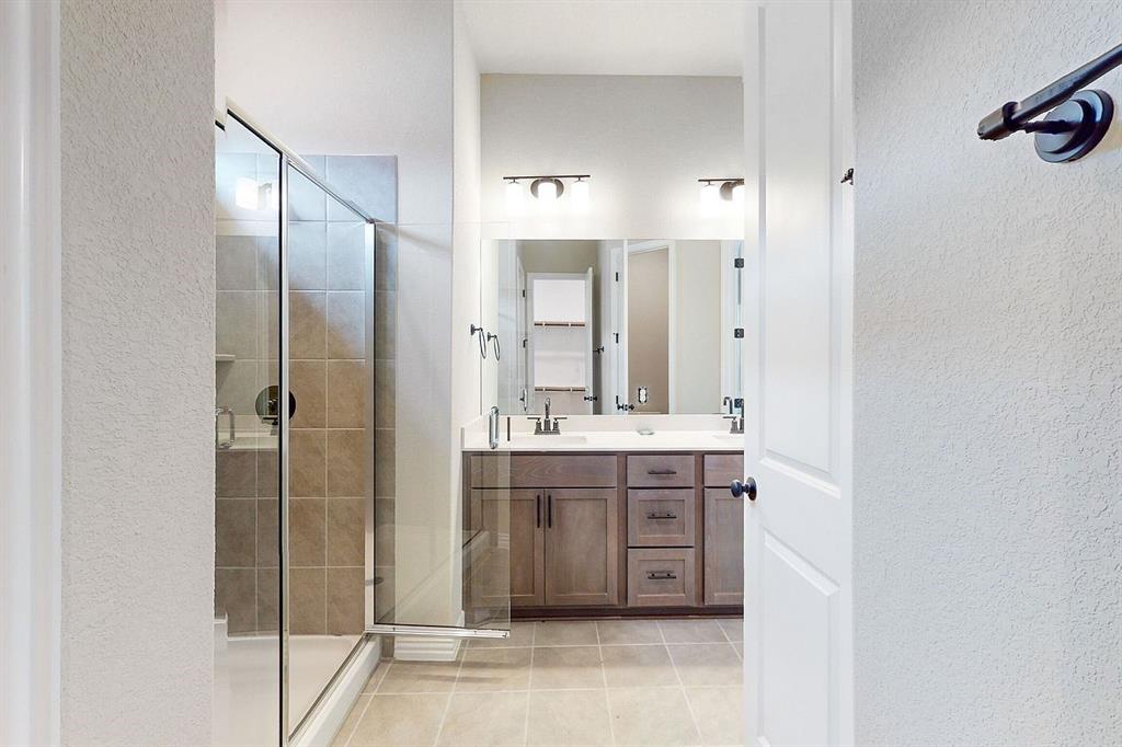 4907 Escape Rivera Drive Austin, TX 78747 - Photo 10 of 28 A well-lit bathroom with a glass-enclosed shower and a dual-sink vanity featuring warm-toned cabinetry.
