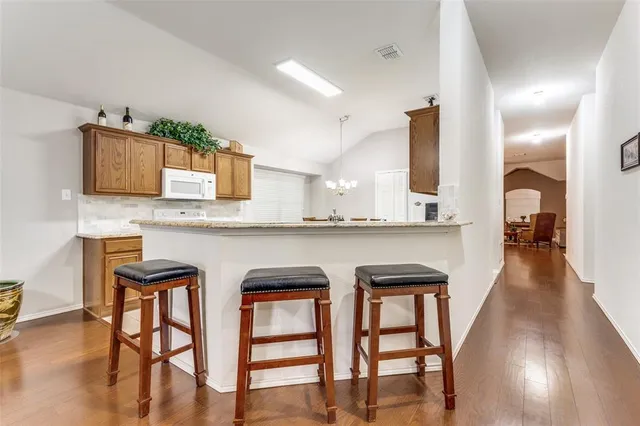 a kitchen with stainless steel appliances granite countertop a stove top oven a sink a dining table and chairs with wooden floor