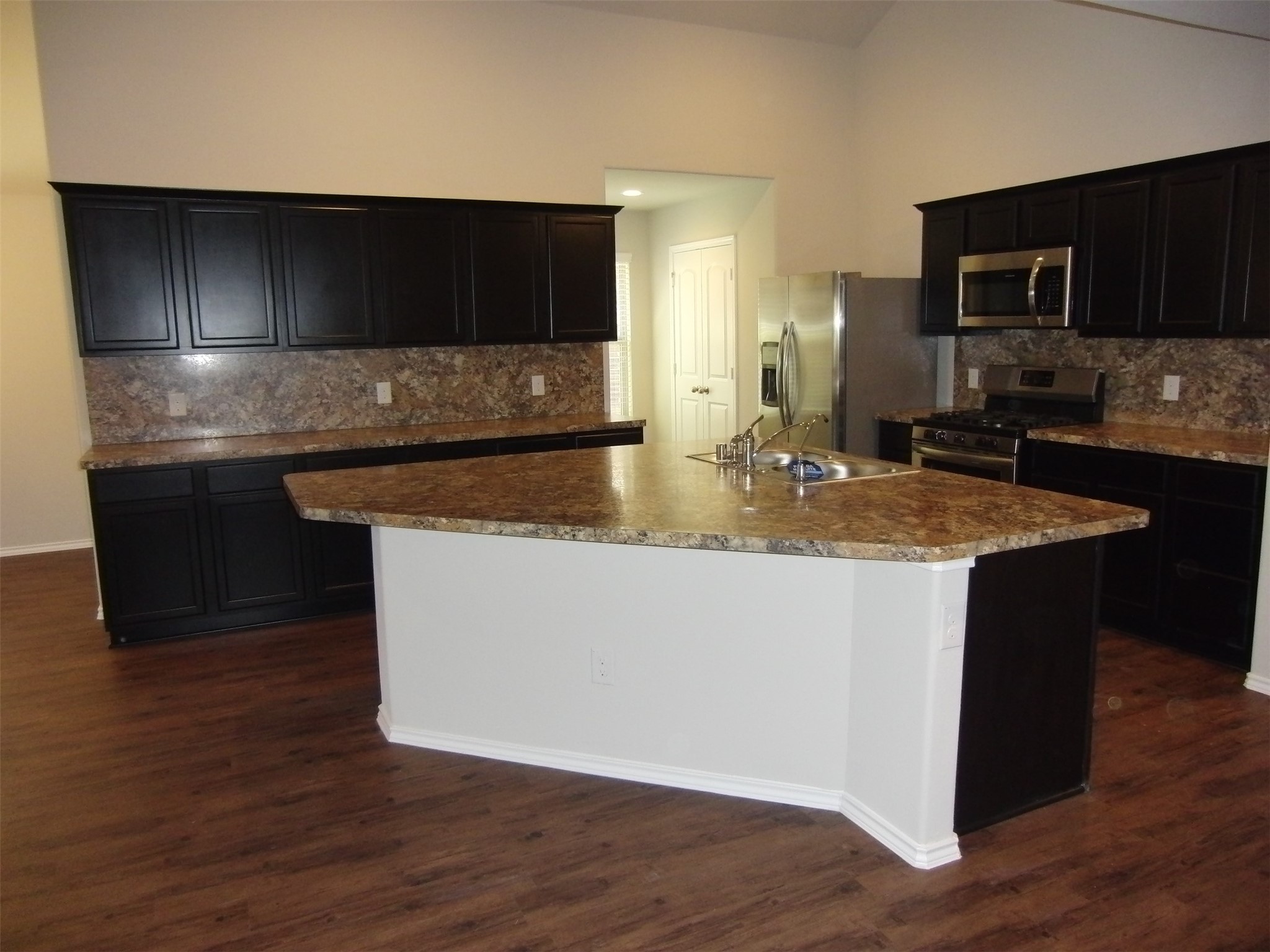 5522 Mesquite Oaks Trail Spring, TX 77389 - Photo 5 of 28 Modern kitchen with dark cabinets, granite countertops, and stainless steel appliances. Features a central island with a sink, ample storage, and wood flooring.