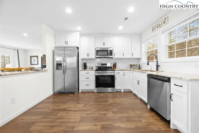 a large kitchen with stainless steel appliances granite countertop a stove a sink dishwasher a refrigerator and a oven with white cabinets