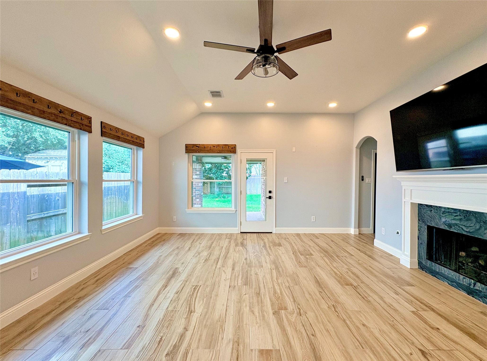 15410 Redbud Berry Way Cypress, TX 77433 - Photo 16 of 49 Bright living room, recessed lighting, and a ceiling fan. Features large windows, hardwood floors, a fireplace, and a mounted TV. Access to the backyard through a door with glass panels.