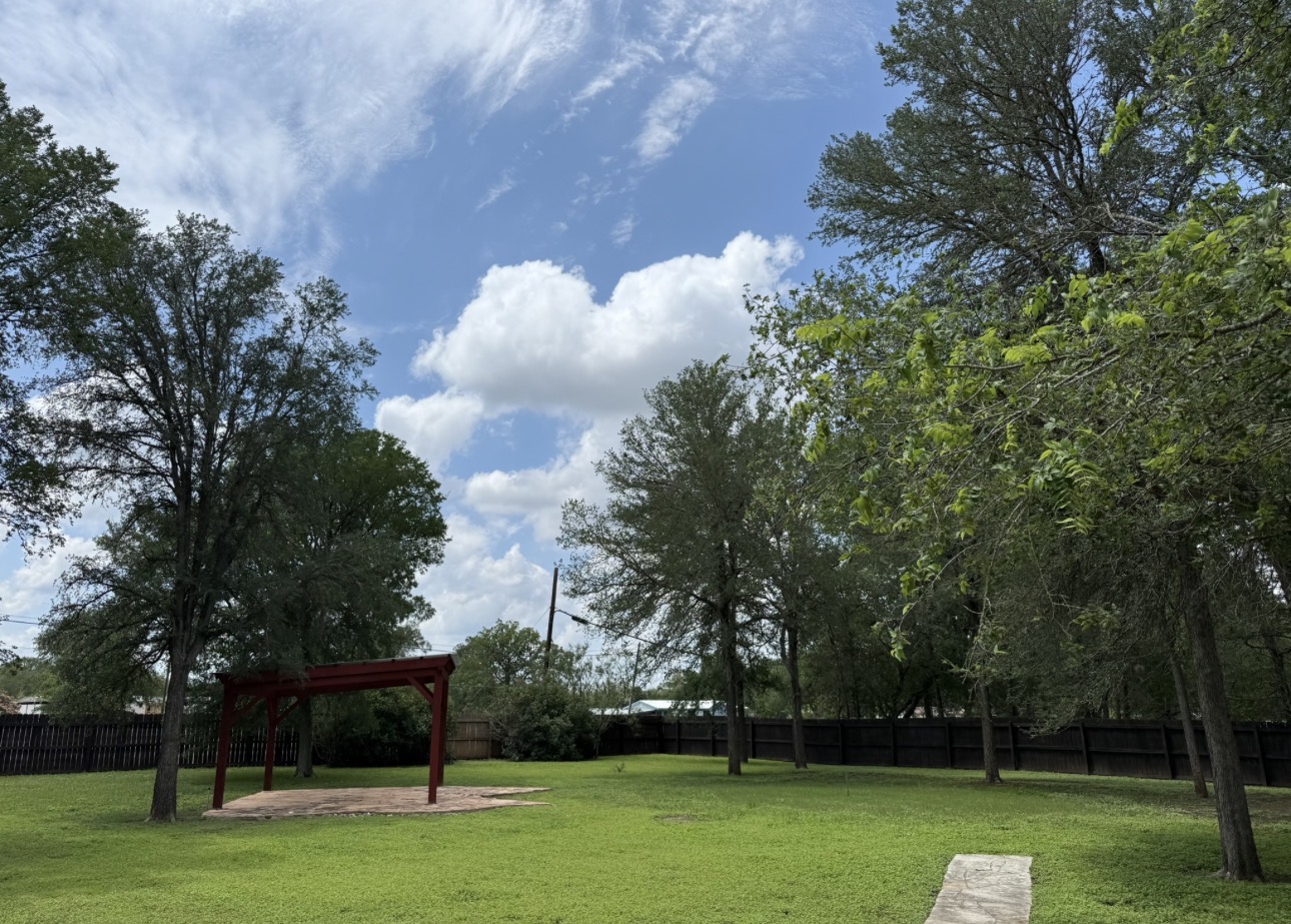 104 Spring Branch Bastrop, TX 78602 - Photo 5 of 32 A spacious yard with mature trees and a charming red pergola offers abundant outdoor living potential.