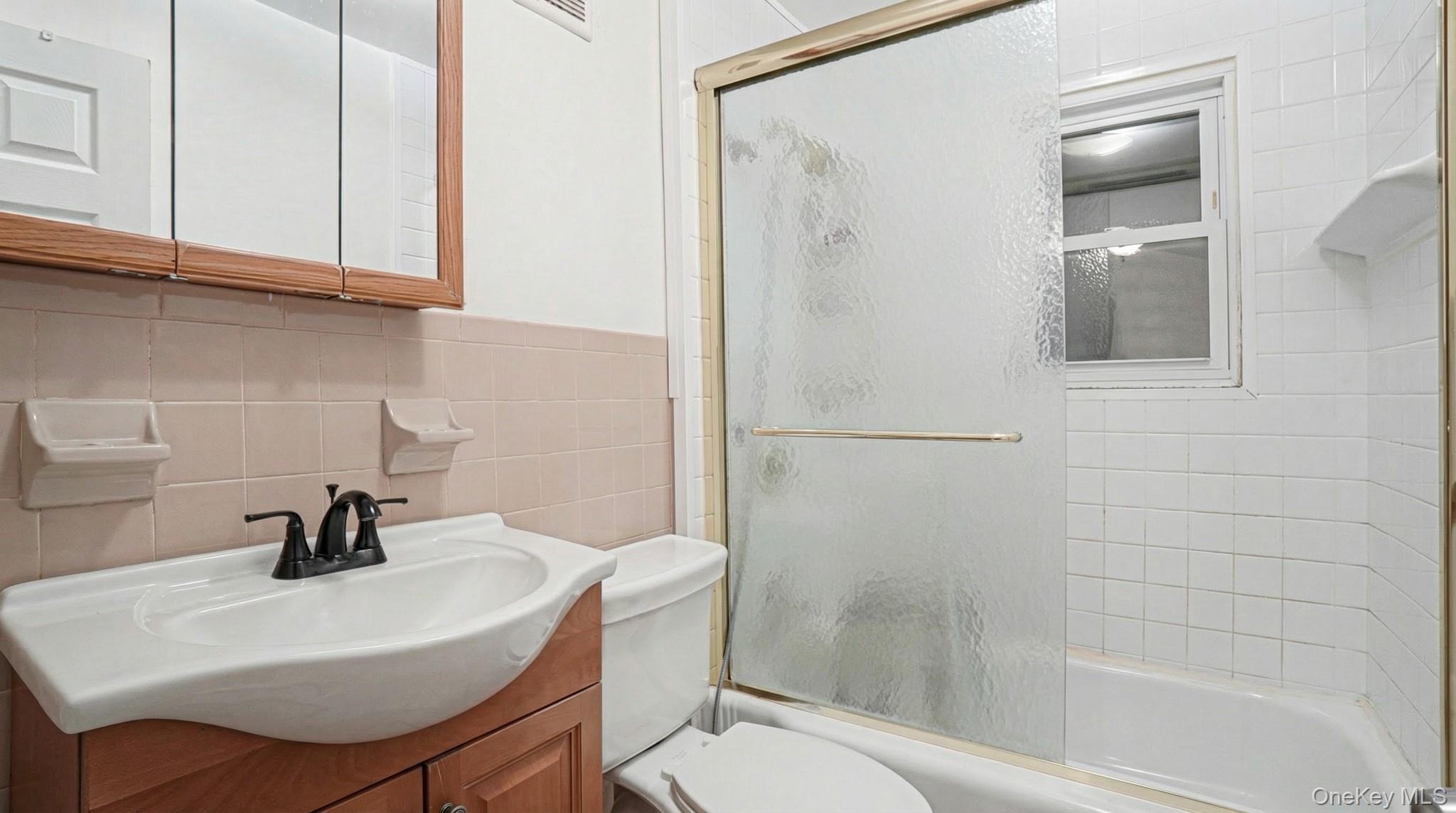 237-09 93rd Road Queens, NY 11426 - Photo 16 of 17 Bathroom featuring vanity, shower / bath combination with glass door, and tile walls