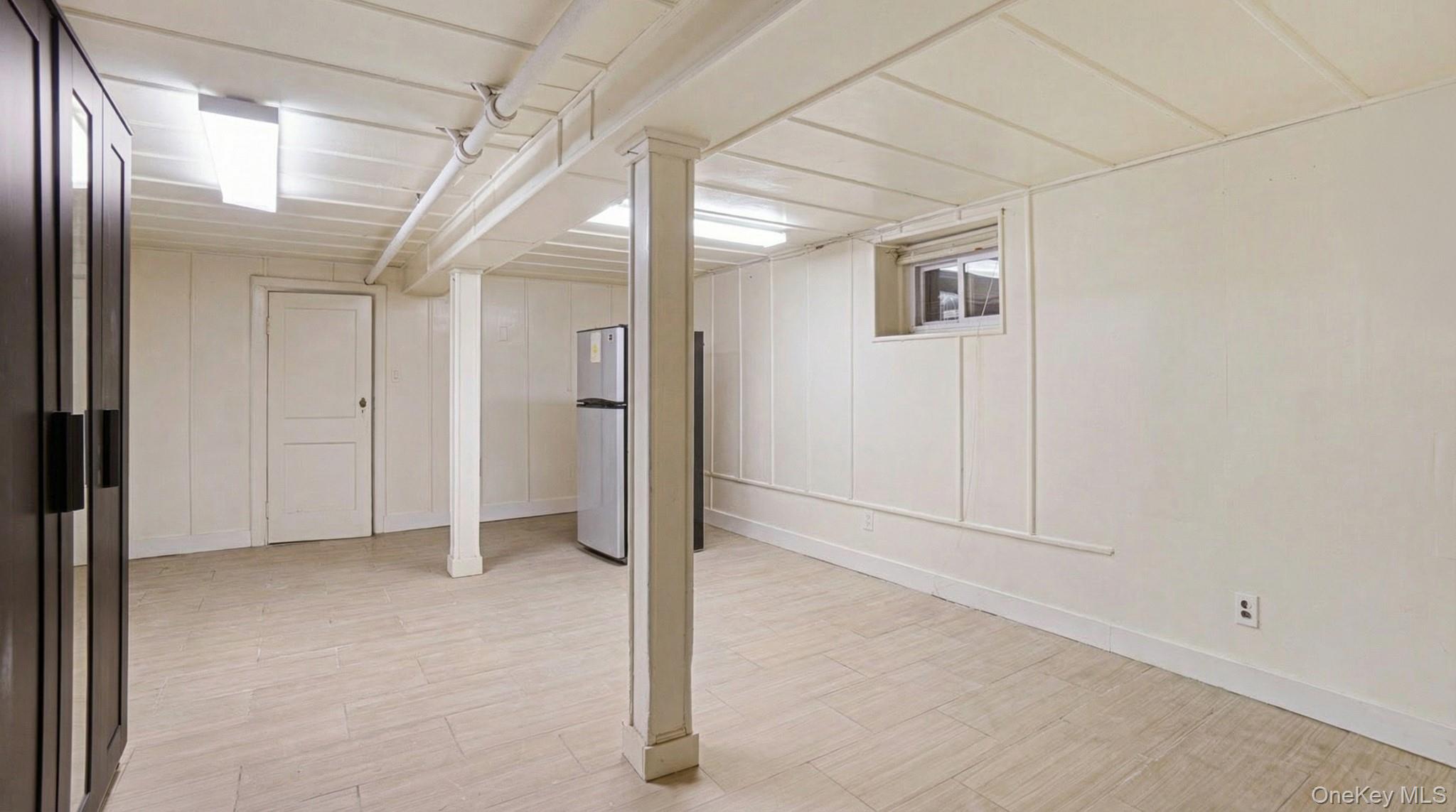 237-09 93rd Road Queens, NY 11426 - Photo 10 of 17 Finished below grade area featuring light wood-style floors, freestanding refrigerator, and a decorative wall