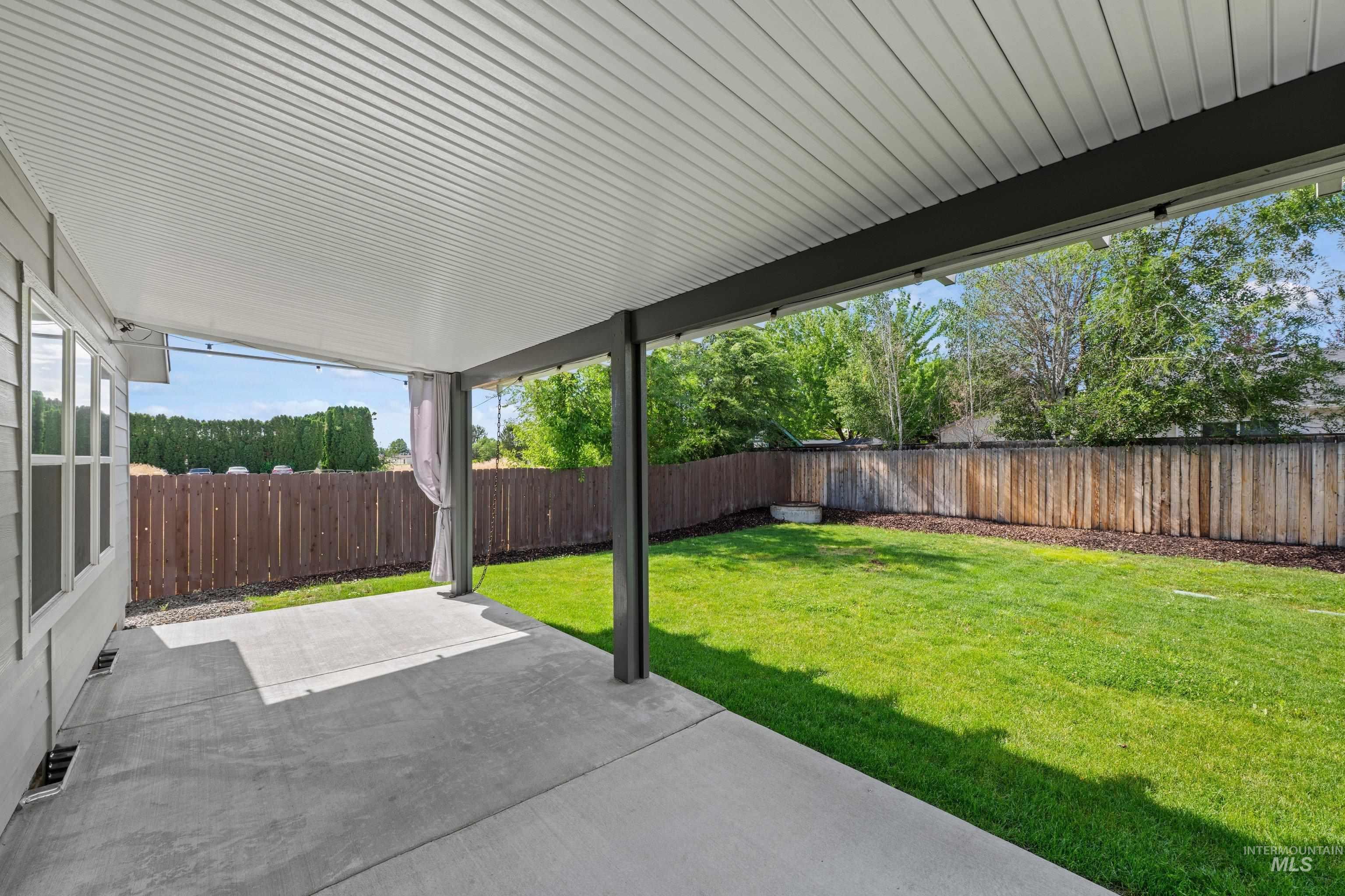 12744 West Fig Street Boise, ID 83713 - Photo 33 of 34 Expansive covered concrete patio featuring a corrugated ceiling, dark support beams, and string lighting