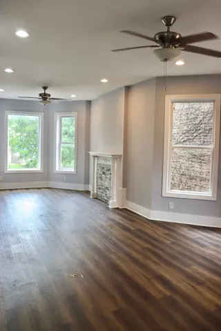 an empty room with wooden floor chandelier fan and windows