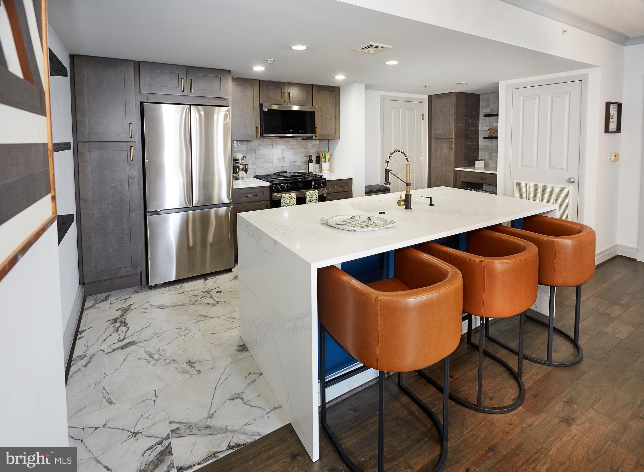 414 Water Street, Unit 2601 Baltimore, MD 21202 - Photo 15 of 51 a kitchen with stainless steel appliances a table chairs and a refrigerator