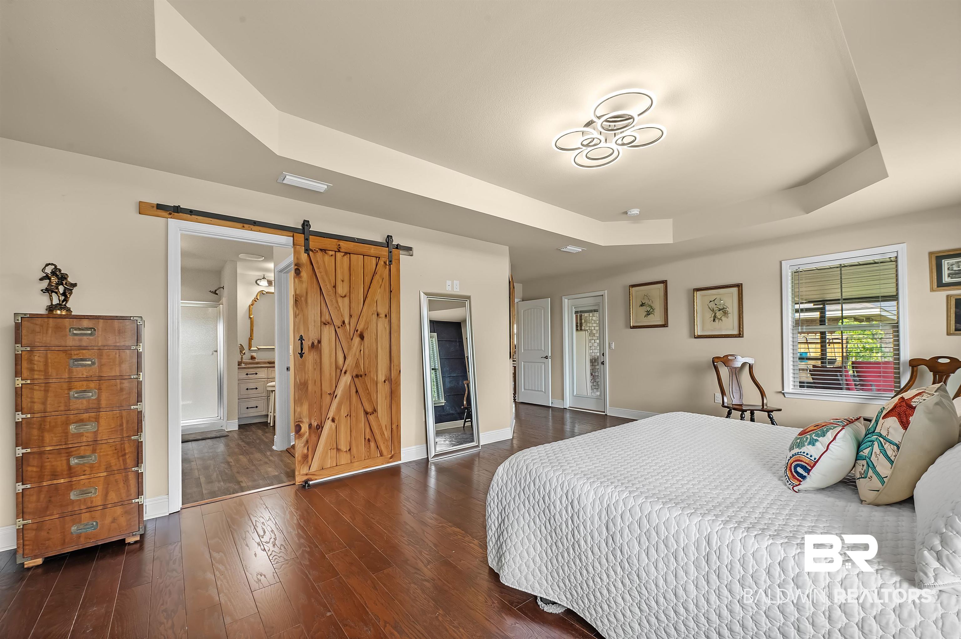 8896 Allay Lane Foley, AL 36535 - Photo 44 of 57 Bedroom with a barn door, a tray ceiling, dark wood-type flooring, and ensuite bath