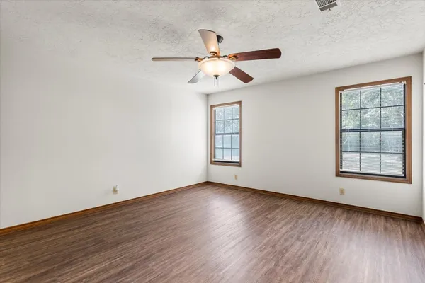 an empty room with wooden floor chandelier fan and windows