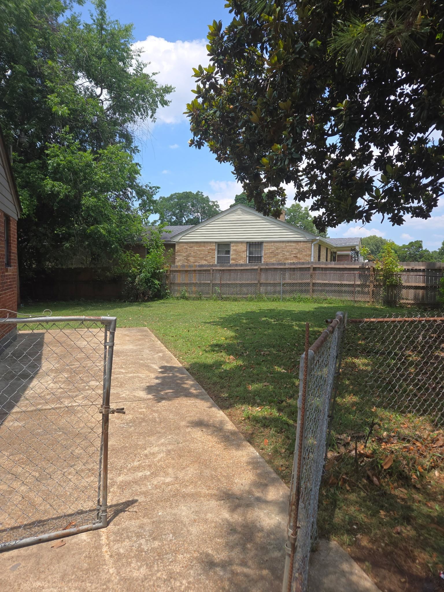 1510 Gausco Road Memphis, TN 38106 - Photo 7 of 10 Expansive grassy yard area with a concrete pathway and chain-link fencing