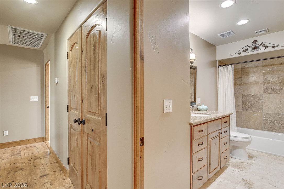 1950 Bowman Road Logandale, NV 89021 - Photo 39 of 81 A well-lit bathroom and hallway feature a rustic knotty wooden door and polished stone flooring.