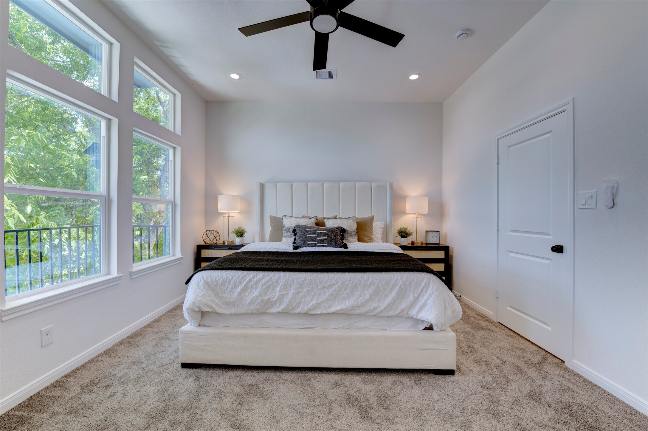 6807 Paris Street Houston, TX 77021 - Photo 26 of 50 Primary bedroom with vaulted ceiling, recessed lighting, ceiling fan, plush carpet, and oversized windows overlooking mature trees. Balcony access visible on left.