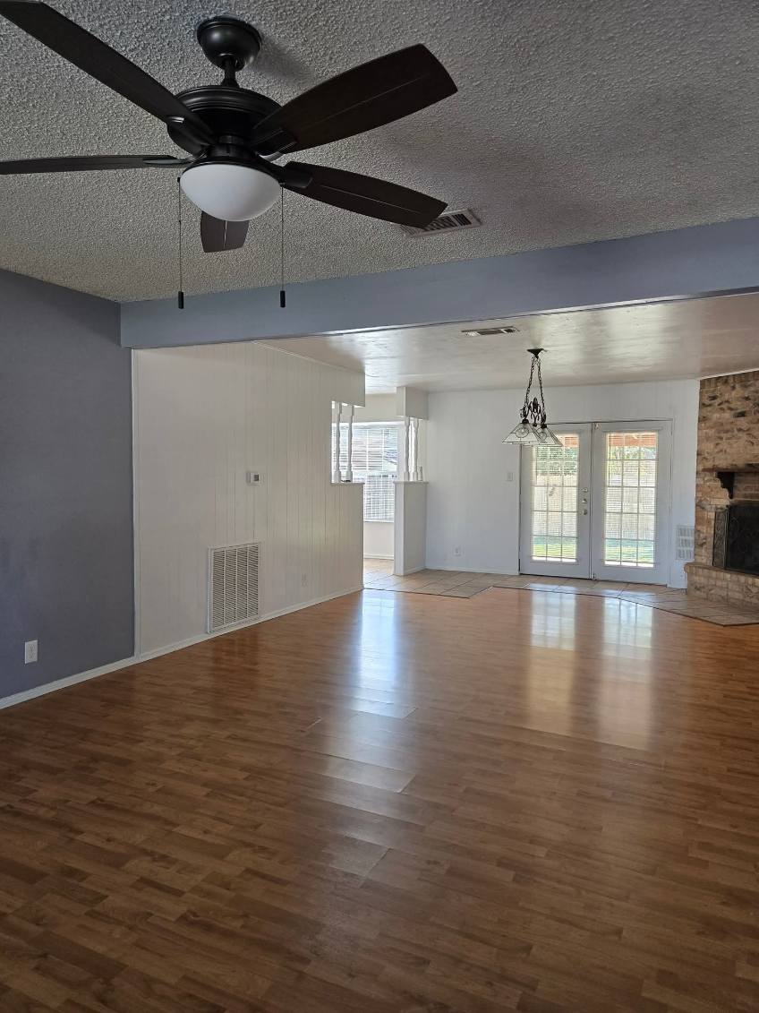 103 Spanish Oak Circle Georgetown, TX 78628 - Photo 2 of 12 Unfurnished living room featuring a textured ceiling, dark wood-style flooring, ceiling fan, french doors, and a large fireplace