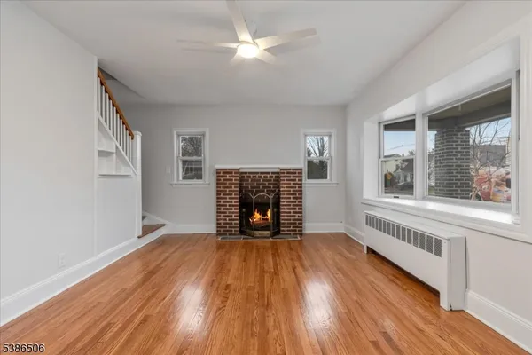 a view of an empty room with wooden floor fireplace and a window