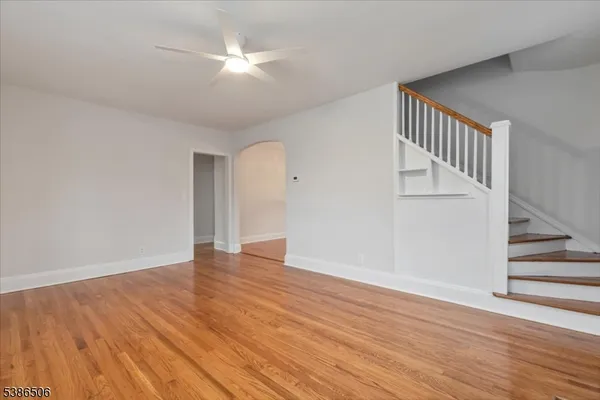 a view of an empty room with wooden floor and a ceiling fan