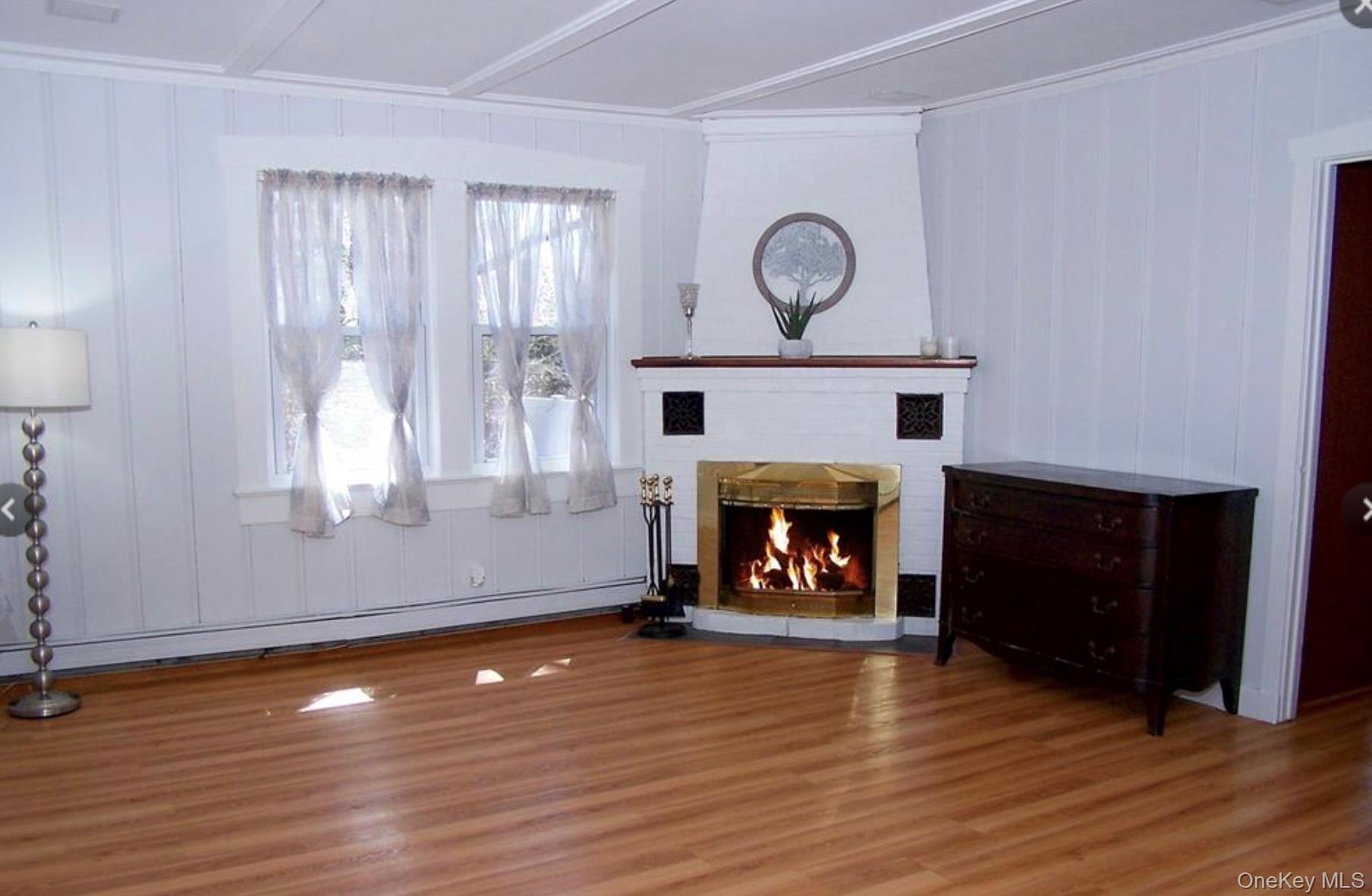 36 Columbine Road Rocky Point, NY 11778 - Photo 3 of 14 Unfurnished living room with a lit fireplace, wood finished floors, baseboard heating, and a decorative wall