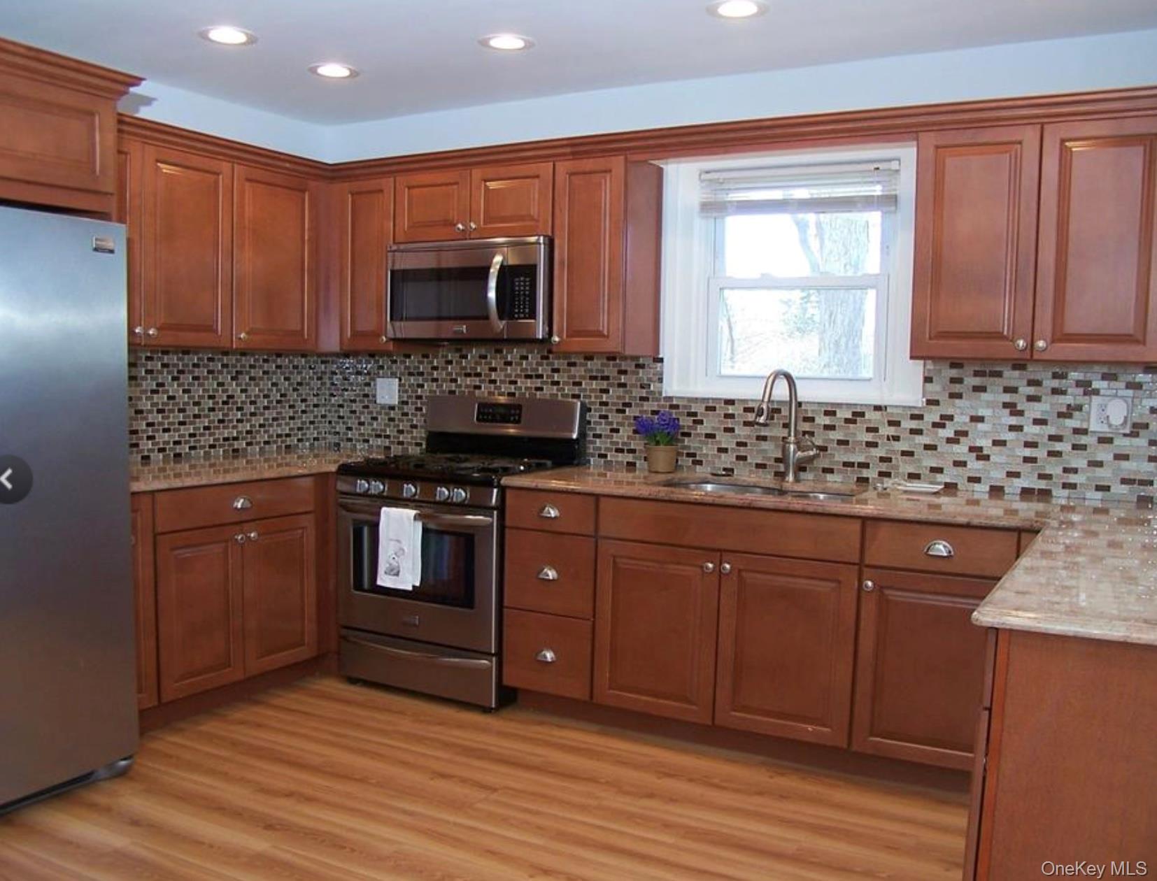 36 Columbine Road Rocky Point, NY 11778 - Photo 6 of 14 Kitchen featuring brown cabinets, appliances with stainless steel finishes, light stone counters, light wood-style flooring, and decorative backsplash