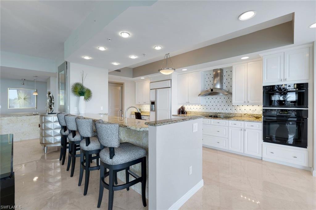 700 La Peninsula Boulevard, Unit 305 Naples, FL 34113 - Photo 12 of 39 a kitchen with stainless steel appliances kitchen island granite countertop a table chairs sink and cabinets