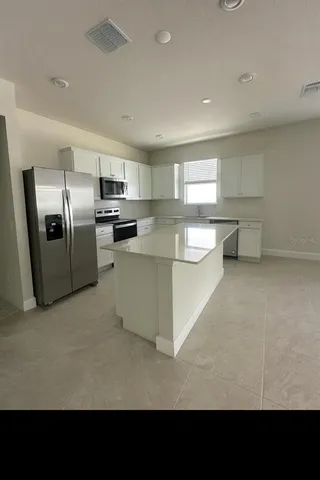 a living room with stainless steel appliances kitchen island granite countertop a refrigerator oven a sink a stove with white cabinets