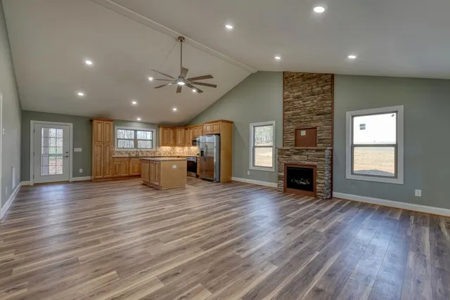an empty room with wooden floor fireplace and kitchen view