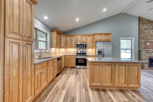 a large kitchen with stainless steel appliances granite countertop a stove a sink dishwasher and a refrigerator with wooden floor