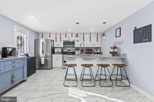 a kitchen with stainless steel appliances kitchen island granite countertop a refrigerator a stove a sink dishwasher and white cabinets with wooden floor