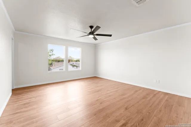 an empty room with wooden floor chandelier fan and windows