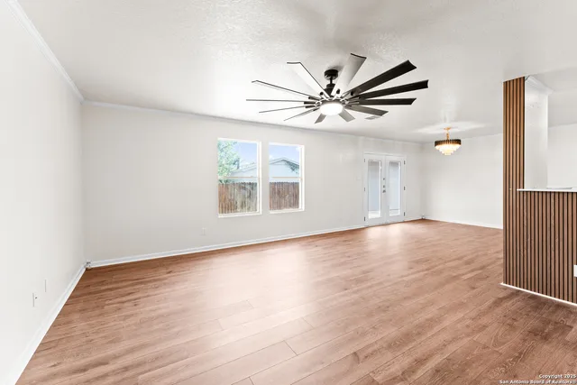 an empty room with wooden floor ceiling fan and windows