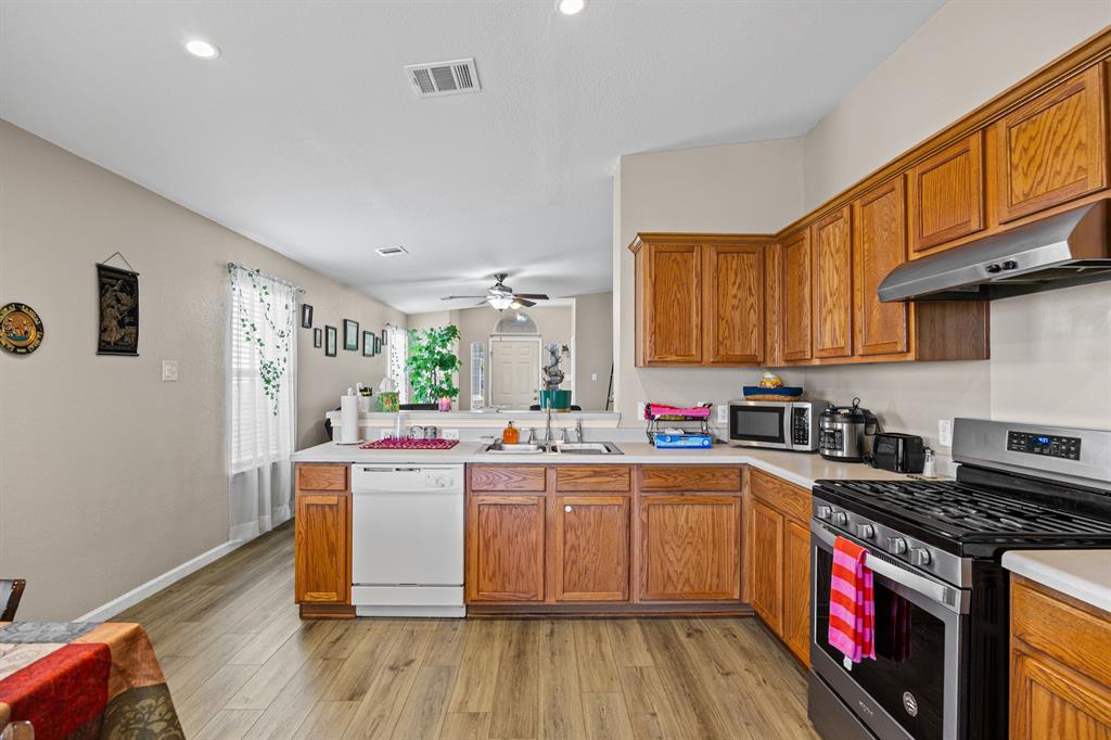 2304 Wilma Rudolph Road Austin, TX 78748 - Photo 7 of 18 Kitchen featuring stainless steel appliances, light countertops, wood finish cabinets, light wood-type flooring, and a peninsula