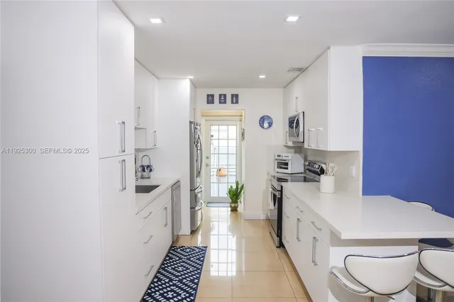 a large white kitchen with sink a stove a refrigerator and white cabinets