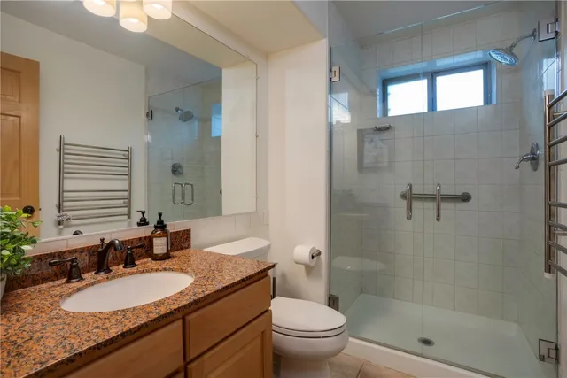 a bathroom with a granite countertop sink a toilet a mirror and shower