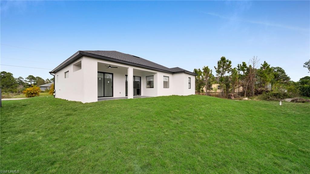 1138 Garibaldi Street East Lehigh Acres, FL 33974 - Photo 31 of 36 Back of property featuring ceiling fan, a patio area, a lawn, and stucco siding