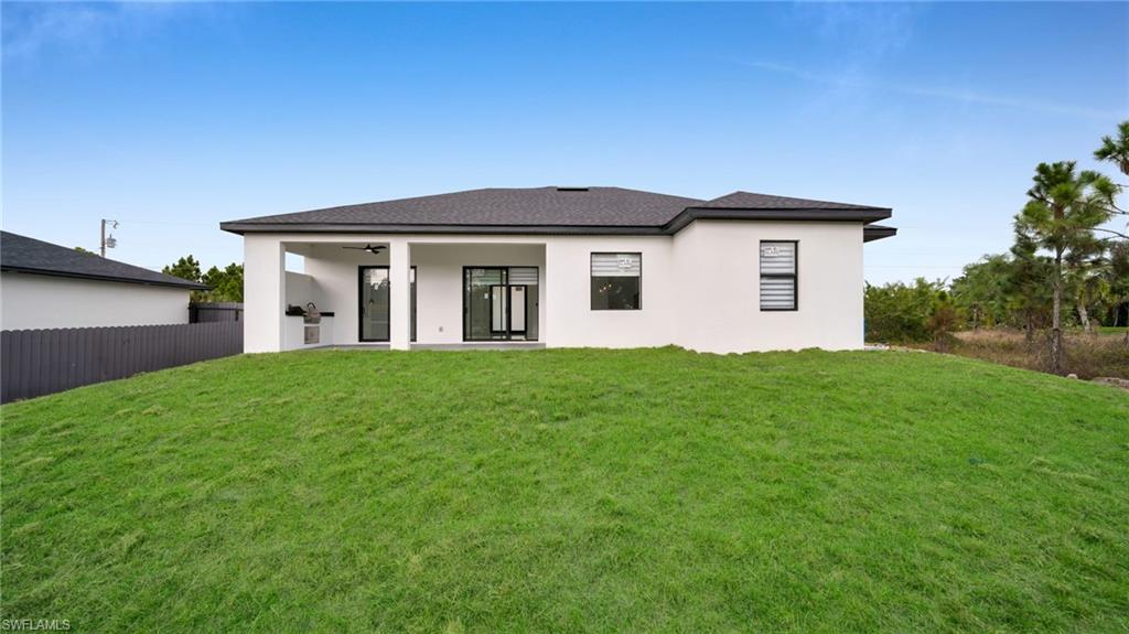 1138 Garibaldi Street East Lehigh Acres, FL 33974 - Photo 32 of 36 Back of property featuring a yard, a patio area, stucco siding, ceiling fan, and a shingled roof