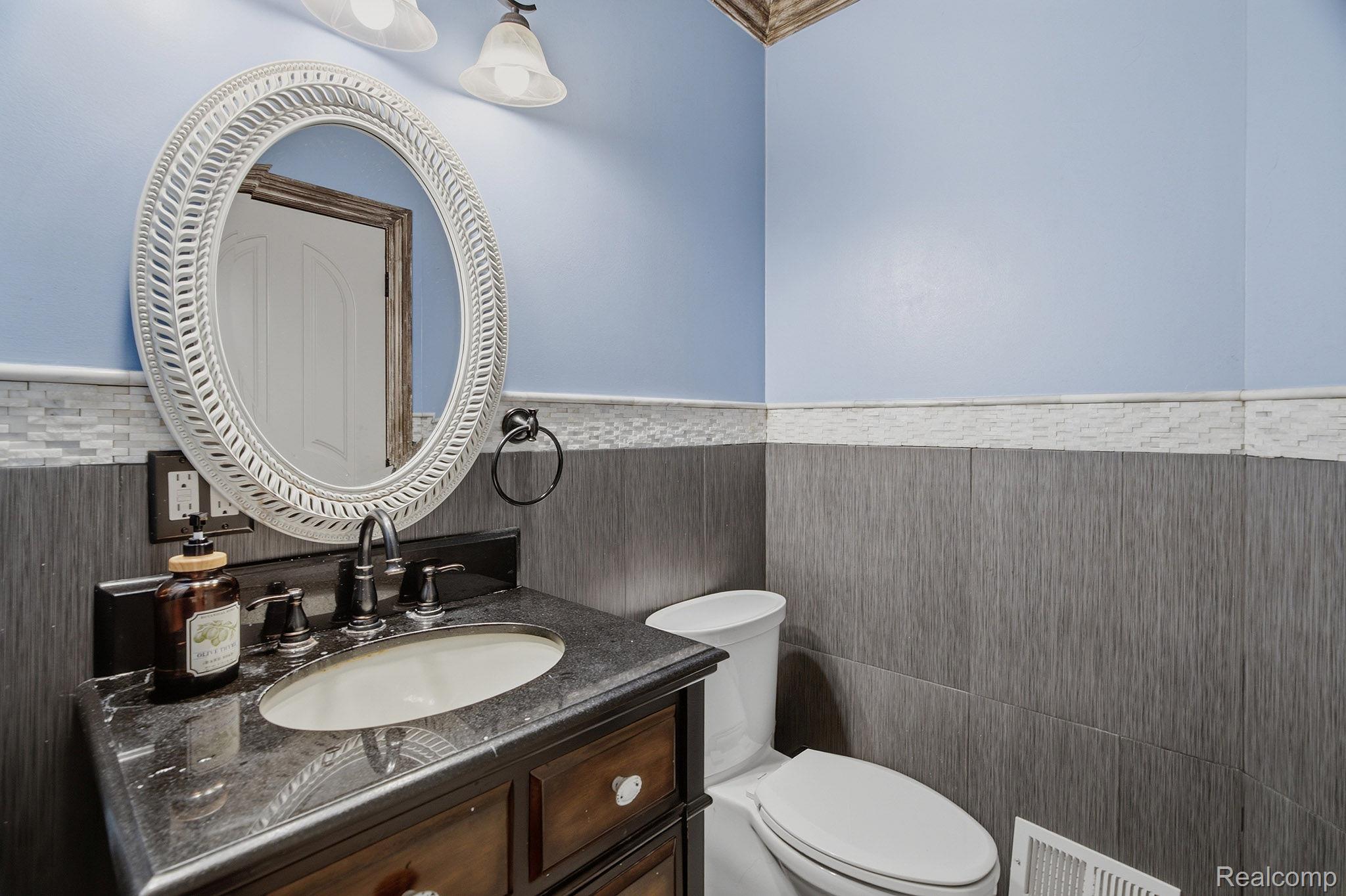 1258 Priscilla Lane Rochester, MI 48309 - Photo 44 of 56 Bathroom featuring a dark wood vanity with a stone countertop, an oval mirror with a decorative frame, a modern toilet, and wainscoting with textured grey tiles and a light-toned mosaic accent