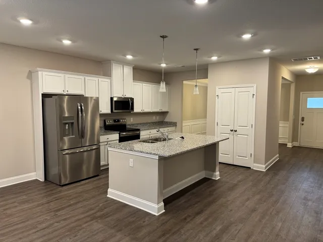 a large kitchen with stainless steel appliances granite countertop a stove a refrigerator a sink and a oven with wooden floor