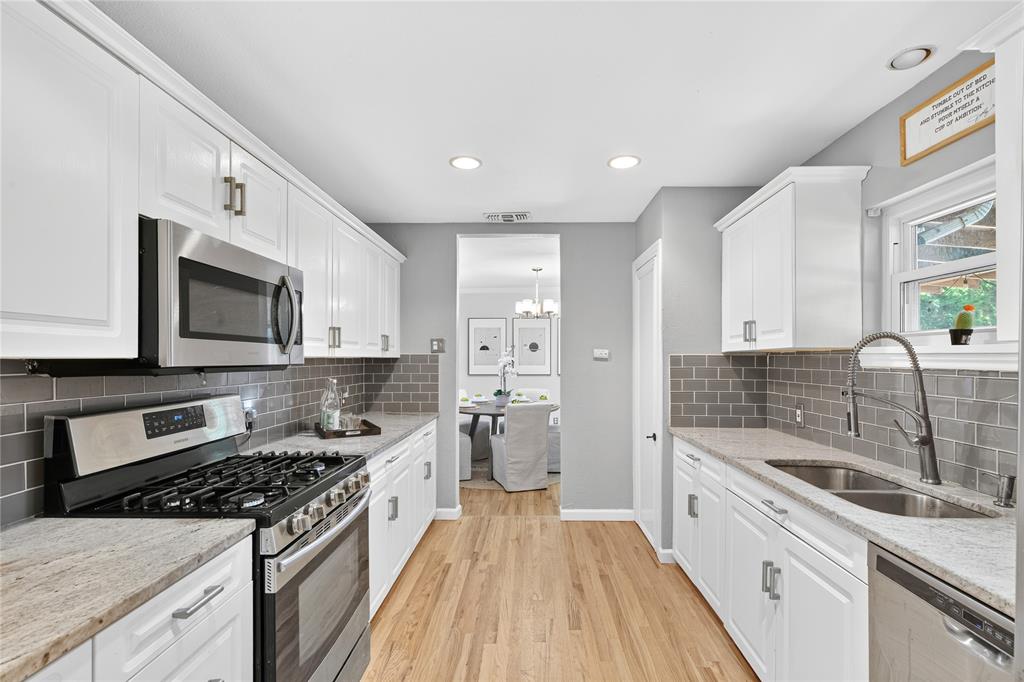 649 Peavy Road Dallas, TX 75218 - Photo 5 of 30 Galley kitchen featuring wood-finish flooring, white cabinetry with silver hardware, light-toned countertops, and a gray subway tile backsplash