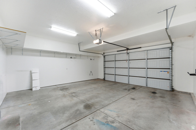 1614 Aspen Loop Provo, UT 84606 - Photo 35 of 47 Spacious two-car garage with a panel garage door, concrete flooring, overhead fluorescent lighting, and built-in wall shelving