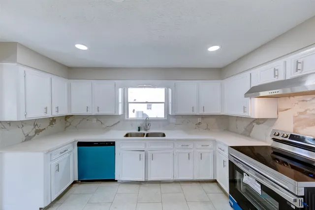 a kitchen with granite countertop a sink stainless steel appliances white cabinets and a window