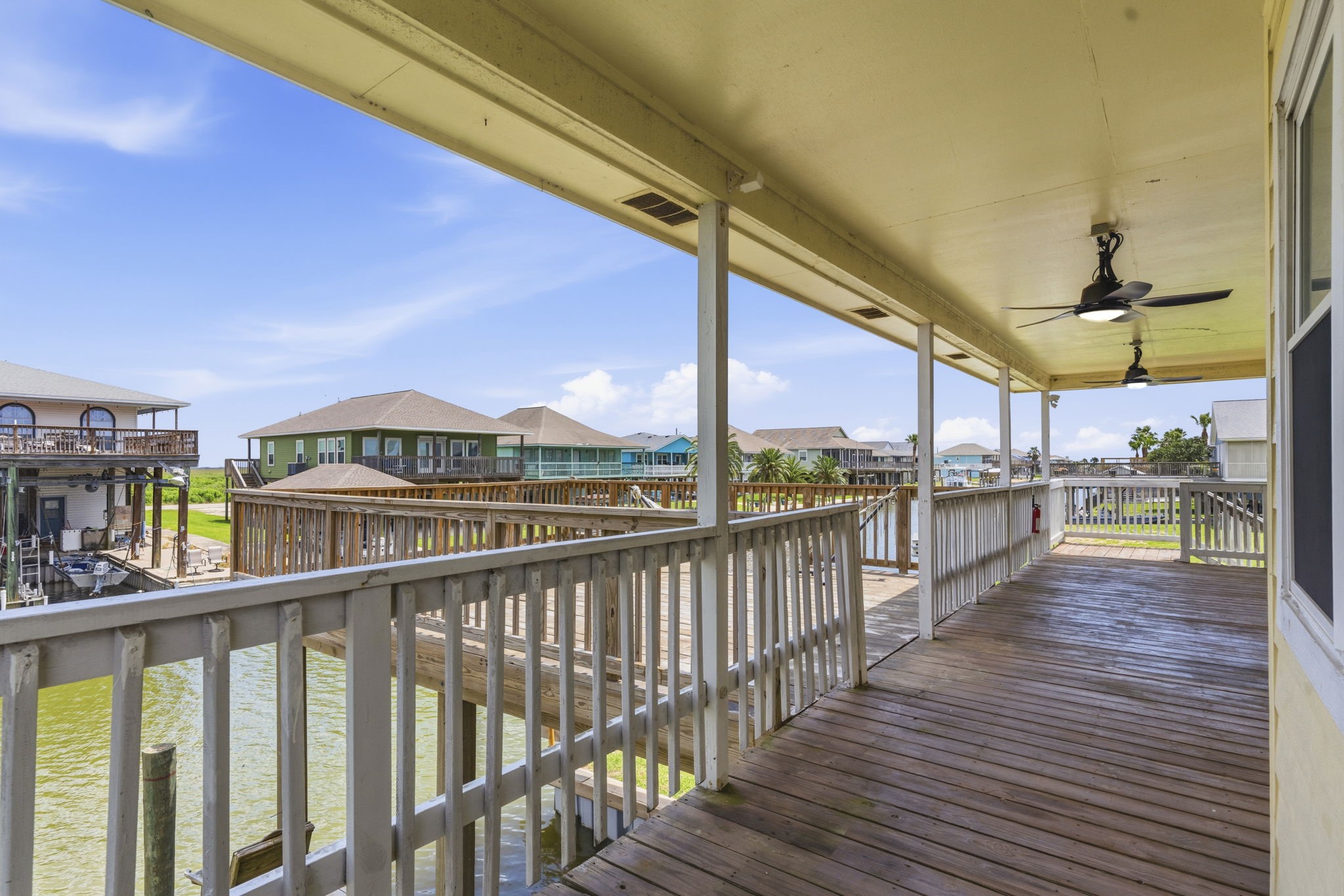 119 Sand Shoals Road Freeport, TX 77541 - Photo 9 of 34 Covered back deck — wood plank decking, white spindle railings, dual ceiling fans, and an open canal view looking toward the bay.