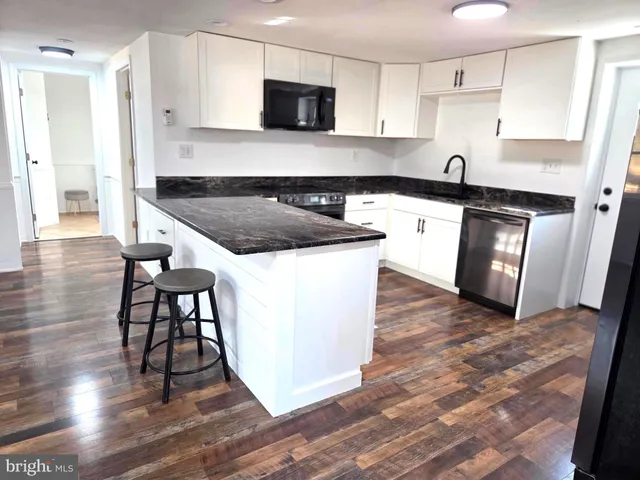 a kitchen with granite countertop a stove top oven a sink dishwasher a refrigerator and white cabinets with wooden floor