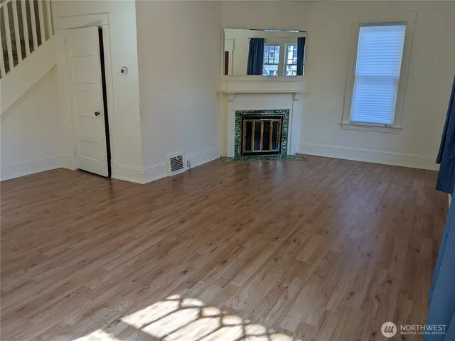 a view of an empty room with wooden floor fireplace and a window