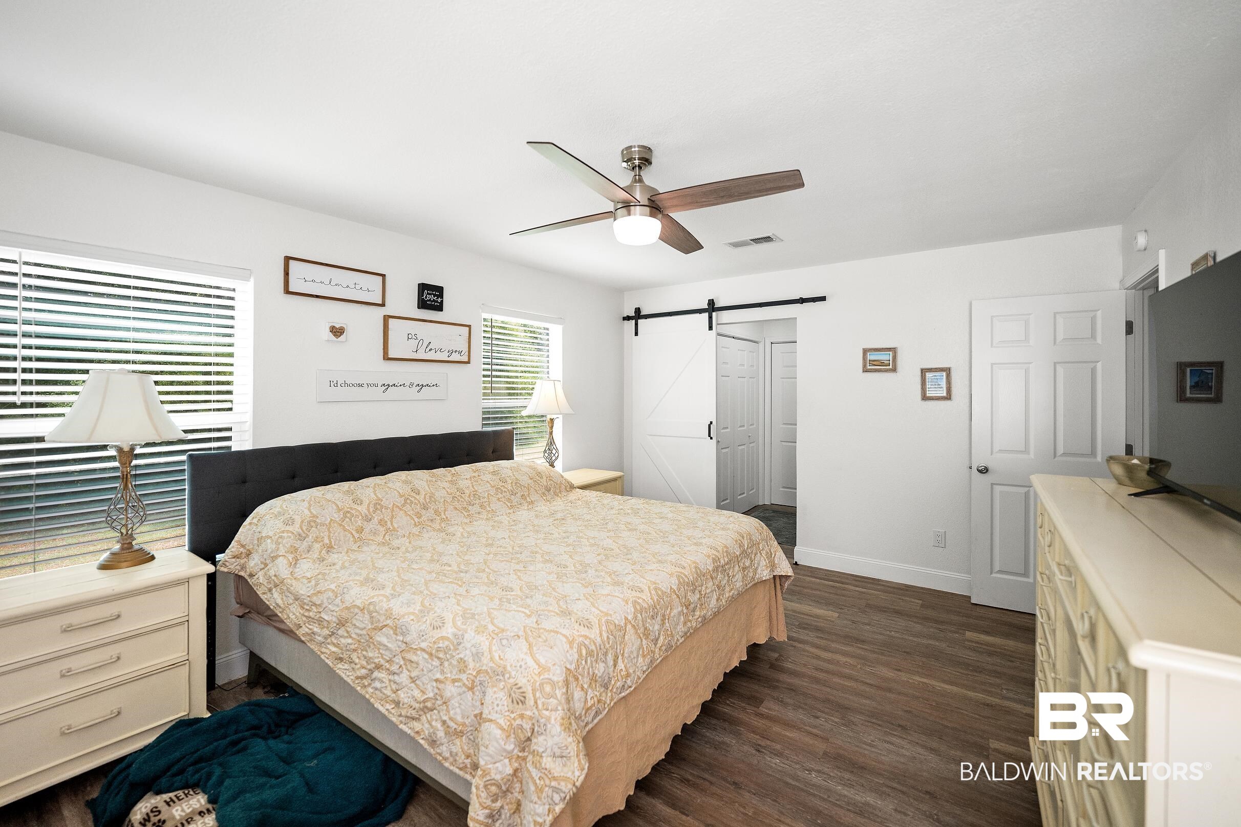 33129 Antietam Road Lillian, AL 36549 - Photo 10 of 31 Spacious room featuring wood-finish flooring, two windows with blinds, a ceiling fan with light, and a white barn door